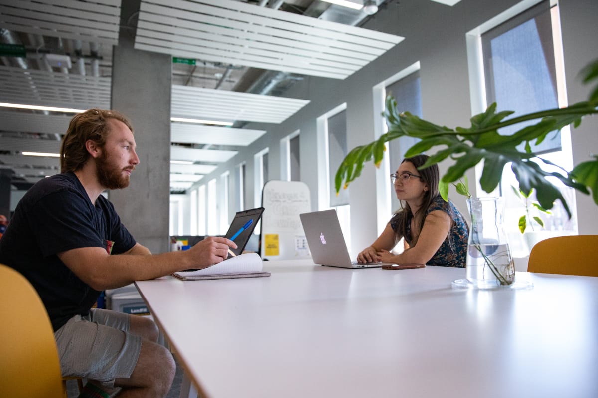 Two people are discussing while sitting on the chairs and having their laptops open